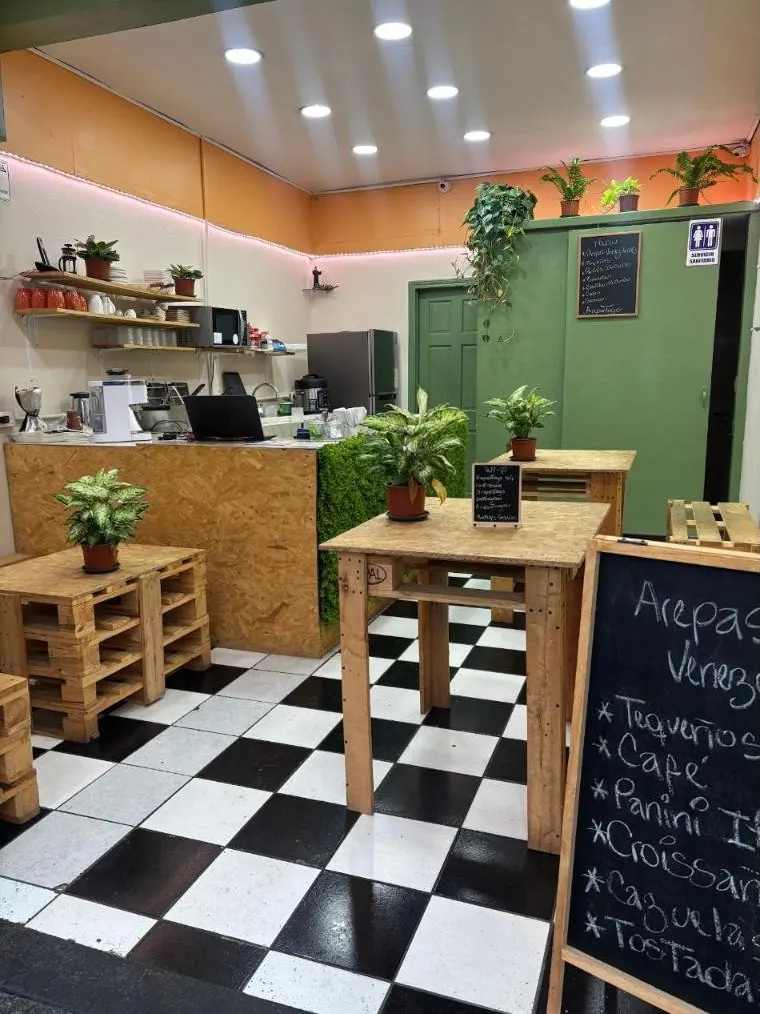 Interior del local de ArepastogoCR con piso a cuadros, muebles de madera y plantas